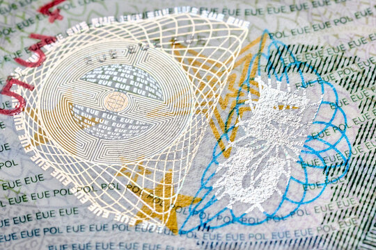 Macro photography shows fragment of Polish Schengen visa with complex security features including hologram, guilloche patterns, microprinting and iridescent silver emblem on textured paper background.