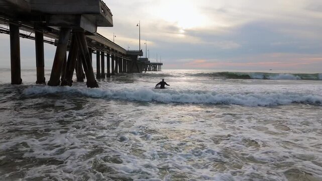 Surfer Paddling Through Waves Near Venice Beach Pier at Sunset California USA