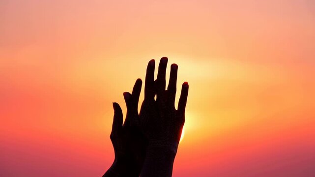 Silhouetted hands opening toward low sunrise sun with glowing rim light, expansive gradient sky, warm backlight, serene spiritual mood, and wide airy composition