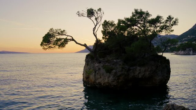 Kamen Brela at sunset in Brela, Croatia, featuring the iconic rocky islet with Mediterranean pine trees overlooking the peaceful Adriatic Sea on the Makarska Riviera