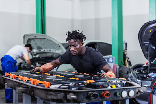 Confident electric vehicle technician smiling beside a high-voltage battery pack during maintenance in a modern EV service center.