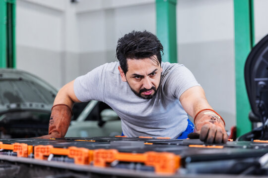 Professional EV technician inspecting high-voltage battery electrical connections inside a modern electric vehicle service center.