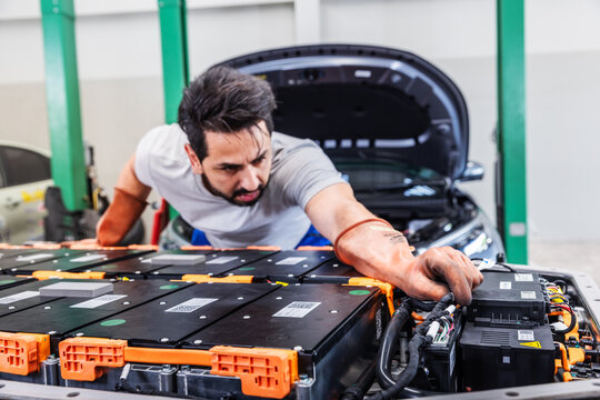 Professional EV technician inspecting high-voltage battery electrical connections inside a modern electric vehicle service center.