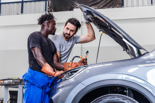 Professional EV technicians inspecting high-voltage electrical cables during maintenance in a modern electric vehicle service workshop.