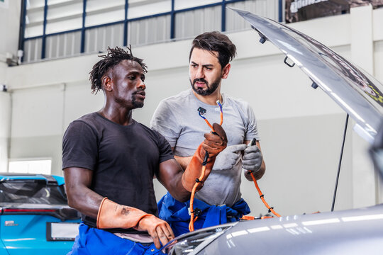 Professional EV technicians inspecting high-voltage electrical cables during maintenance in a modern electric vehicle service workshop.