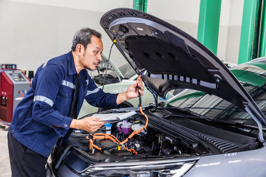 Experienced senior technician inspecting a high-voltage electrical connector inside an electric vehicle during maintenance in a modern EV service workshop. Concept of electric vehicle diagnostics