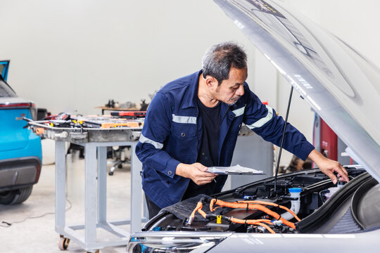 Experienced senior automotive technician using a professional diagnostic scanner to inspect an electric vehicle in a modern EV service center.