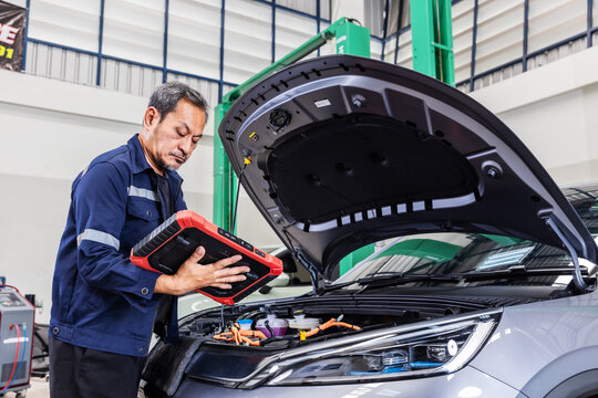 Experienced senior automotive technician using a professional diagnostic scanner to inspect an electric vehicle in a modern EV service center.