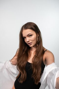Young woman with long brown hair taking a lifestyle selfie, posing in a black bodysuit and white shirt