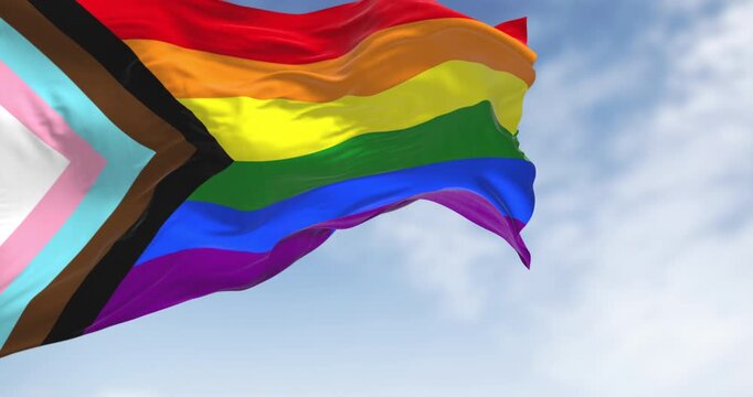 Progress Pride Flag waving against cloudy blue sky