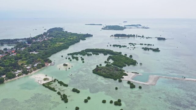 Aerial view of a tropical island archipelago surrounded by clear turquoise sea and coral reefs. Drone shot of an island strip with green trees in the ocean. Pari island in Indonesia 