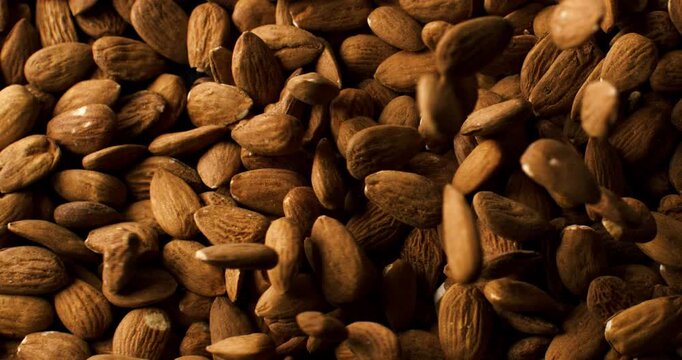 Whole almonds falling onto a pile in slow motion with warm lighting.