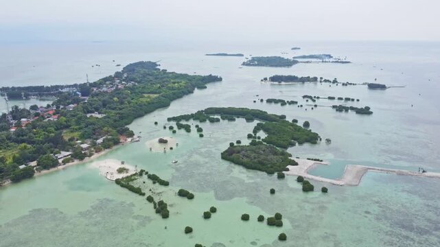 Aerial view of a tropical island archipelago surrounded by clear turquoise sea and coral reefs. Drone shot of an island strip with green trees in the ocean. Pari island in Indonesia 