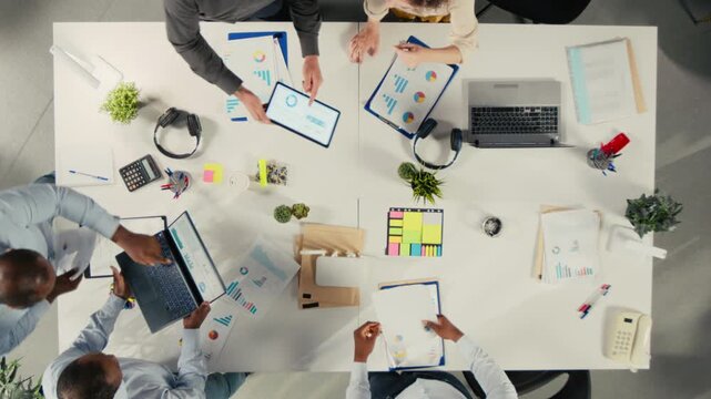 Professional staff assess business objectives from an overhead angle in a shared office, using reports and performance data to align targets with management goals.