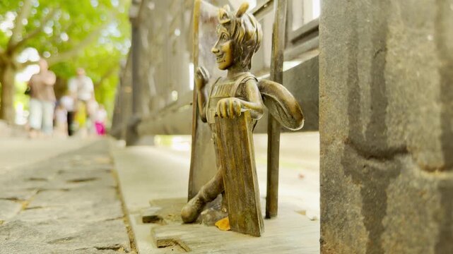 A small bronze bee figurine stands cheerily on a bridge railing in Simferopol, Crimea. Its playful pose brings sense of wonder and fun to the sunny city park walkway, creating a delightful experience.