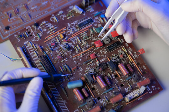 A technician uses tweezers and a multimeter to fix electronic components on a circuit board in a lab