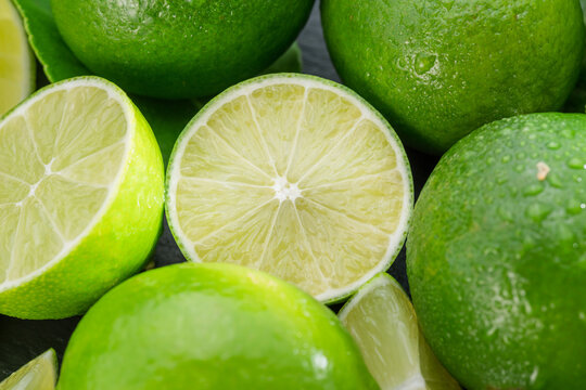 Ripe lime fruits with slices and lime leaves on a gray stone table.