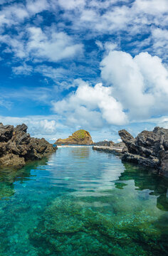 Crystal clear turquoise water inside the natural volcanic rock swimming pools under a bright blue sky in Porto Moniz, Madeira, Portugal.