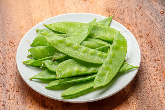 Top view of a heap of fresh green snow peas served on a white ceramic plate