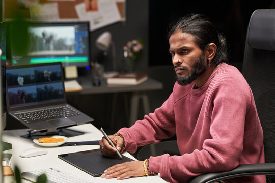 Young Indian man editing video with pen tablet at workstation, focusing on post production workflow and digital content creation. For media agency, creative studio, remote work marketing