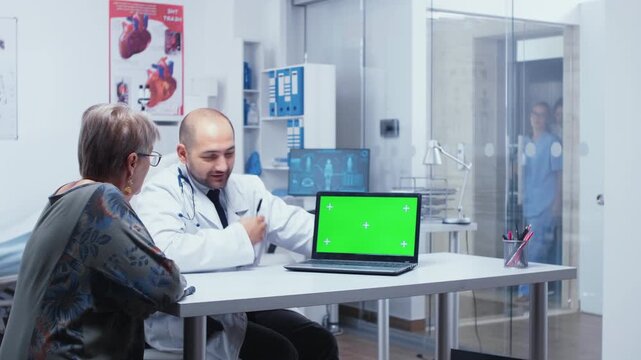 Doctor holds a green screen consultation in a modern private clinic, using a replaceable screen mockup as a healthcare app interface or advertising mockup.