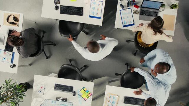 Professional staff use laptops and computers from an overhead angle in a corporate workspace, using digital reports and charts to analyze information for office decisions.