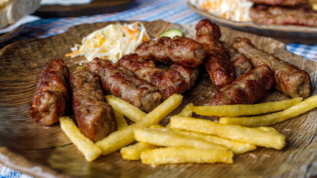 Cevapi served with fries and cole slaw on a wooden plate in a restaurant setting
