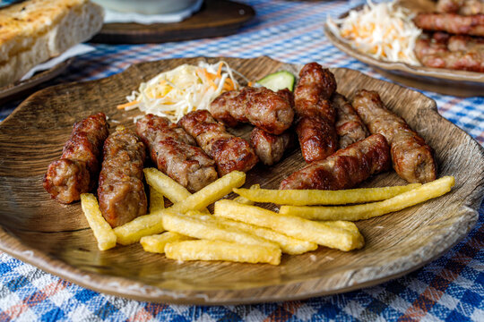Cevapi served with fries and salad on a wooden plate at a local eatery during lunch time
