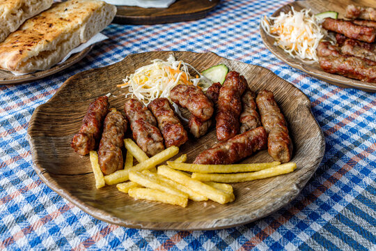 Cevapi served with fries and salad on wooden plates at a dining table outdoors