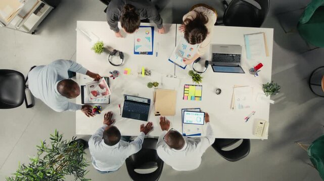 Corporate employees review forecasting data from an overhead angle in a shared office, where forecasting data help them connect analytics with management goals.