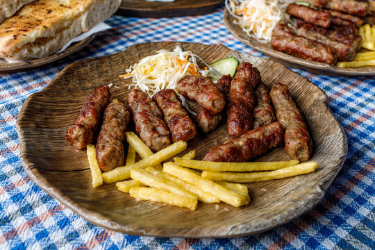 Delicious cevapi served with fries and salad on a wooden plate in a casual dining setting