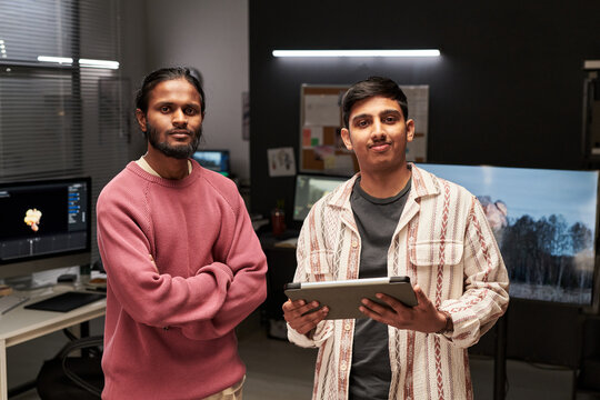 Portrait of two male colleagues standing in digital studio, holding tablet and collaborating on media project. Ideal for creative team, startup, tech workplace marketing