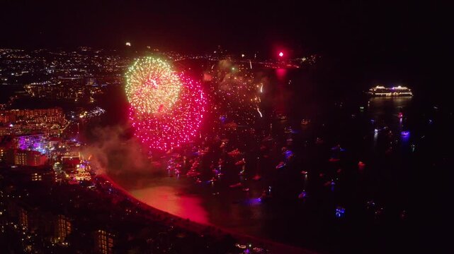 4K drone footage capturing massive fireworks exploding over the scenic bay and city lights of Cabo San Lucas during New Years Eve; Los Cabos, Baja California Sur, Mexico.
