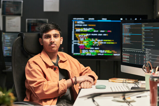 Portrait of young Asian man sitting at workstation, developing software with code on multiple monitors. Ideal for cybersecurity, programming, tech career, remote work marketing