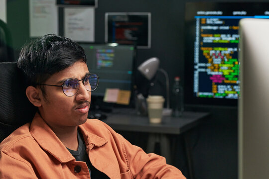 Asian web engineer coding at desktop workstation, monitoring software development screens in office. Technology career, programming, cybersecurity, IT recruitment use, medium shot