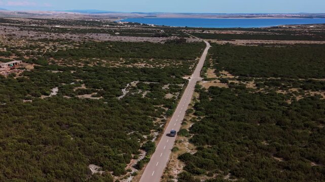 Camper van car driving on a road toward the blue Adriatic Sea, Pag Island, Croatia. Aerial view