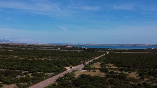 Silver camper van car driving down a long road toward the Adriatic Sea on Pag Island, Croatia. Aerial