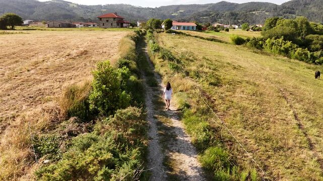 Aerial view of a model released woman walking a country lane toward village houses