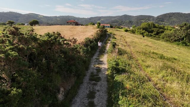 Drone view of a model released woman walking toward houses through rural fields