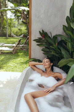 Relaxed Woman Enjoying a Luxurious Outdoor Bubble Bath in Tropical Setting