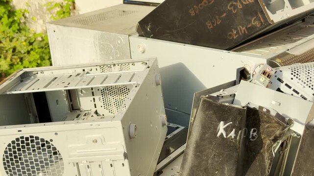 Discarded computer cases sit in a messy pile outdoors. This abandoned hardware creates a sad feeling of neglect and obsolescence for past technology.