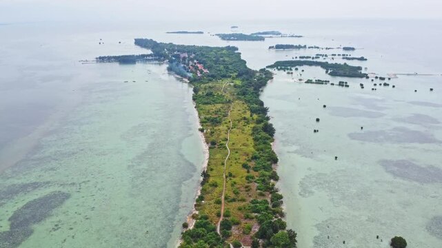 Aerial view of a tropical island archipelago surrounded by clear turquoise sea and coral reefs. Drone shot of an island strip with green trees in the ocean. Pari island in Indonesia 