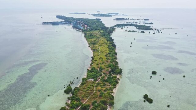 Aerial view of a tropical island archipelago surrounded by clear turquoise sea and coral reefs. Drone shot of an island strip with green trees in the ocean. Pari island in Indonesia 