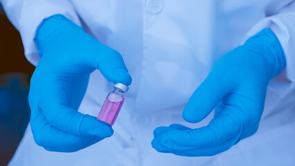 Fototapeta premium Scientist wearing gloves holding a medical vial with pink liquid solution