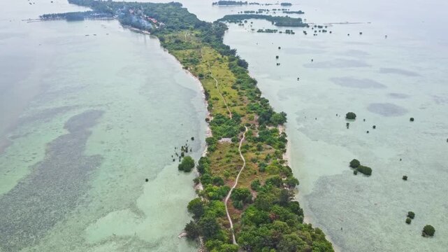 Aerial view of a tropical island archipelago surrounded by clear turquoise sea and coral reefs. Drone shot of an island strip with green trees in the ocean. Pari island in Indonesia 