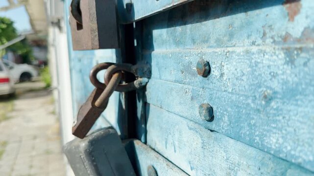 Heavy padlocks secure a weathered blue door. This sturdy barrier evokes feelings of quiet isolation, mystery, and a nostalgic sense of safety in an old, forgotten place.