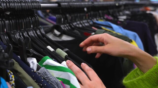 Close-up of female hands browsing clothing on a rack in a second-hand shop, representing eco-friendly shopping, sustainable lifestyle, circular economy, and mindful fashion choices.
