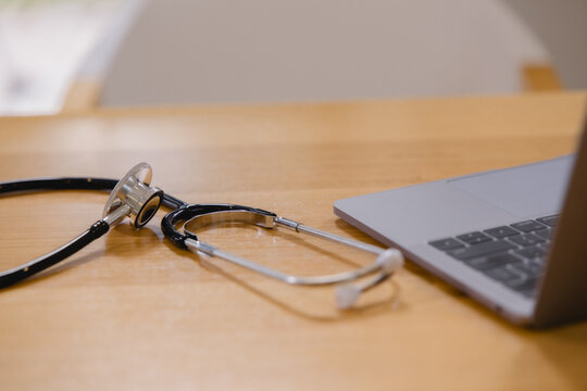 stethoscope on a wooden desk beside a laptop in a modern medical office. Healthcare equipment symbolizing medical care, clinical practice, telemedicine, professionalism and health services.
