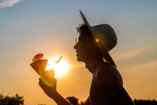 Person holding watermelon drink with straw and umbrella against summer sunset sky
