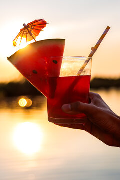 Hand holding refreshing watermelon cocktail during warm summer sunset